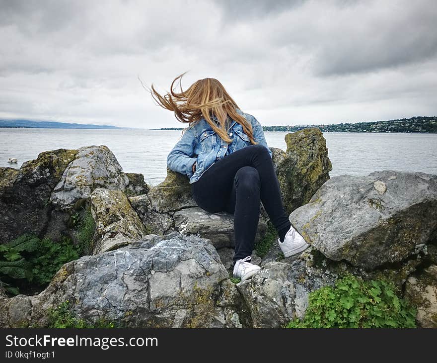 Woman With Blue Denim Collared Button-up Jacket and Black Jeans Sitting on Gray Rock Watching Lakeview