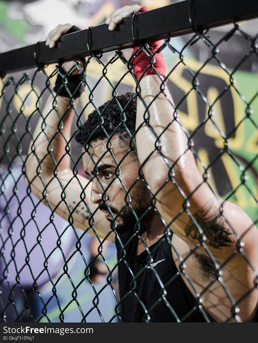 Man Wearing Black Tank Top While Holding Fence