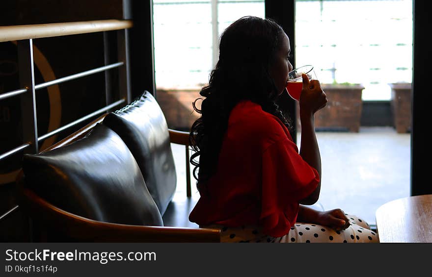 Woman Wearing Red Long-sleeved Blouse Sitting and Drinking Liquid