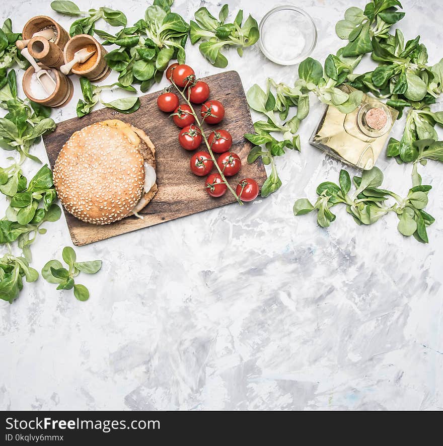 Cooking a homemade burger with chicken cutlet, and a side dish of salad with cherry tomatoes, seasonings and oil, on a white rustic vintage background place for text. Cooking a homemade burger with chicken cutlet, and a side dish of salad with cherry tomatoes, seasonings and oil, on a white rustic vintage background place for text