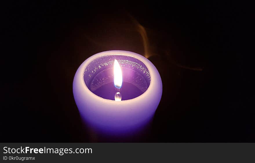 Flame reflection in the liquid wax of purple candle in the black darkness with touch of smoke. Candlelight flame closeup. Burning fire of single purple candle in darkness. Reflection of glowing flame in liquid wax of violet candle. Cylinder shape candle with round top closeup. . Flame reflection in the liquid wax of purple candle in the black darkness with touch of smoke. Candlelight flame closeup. Burning fire of single purple candle in darkness. Reflection of glowing flame in liquid wax of violet candle. Cylinder shape candle with round top closeup.