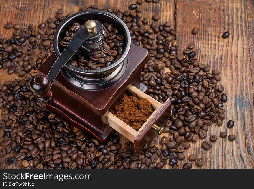 Coffee mill on rustic wooden plank background and roasted coffee beans