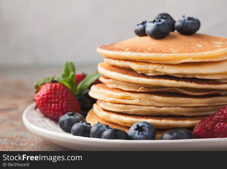 Close-up delicious pancakes, with fresh blueberries, strawberries and maple syrup on a rusty background. With copy space