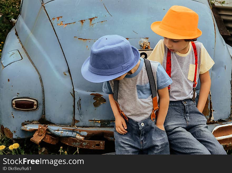 Two Boy in Grey Shirts and Blue Overall Pants Sitting on Blue Car Bumper