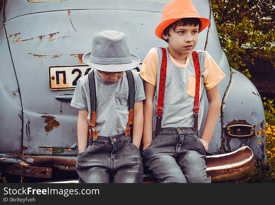 Two Boys Wearing Gray Shirts Sitting on Gray Vehicle Bumper