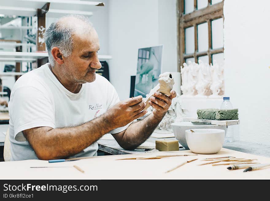 Man in White Crew-neck T-shirt Holding White Figurine