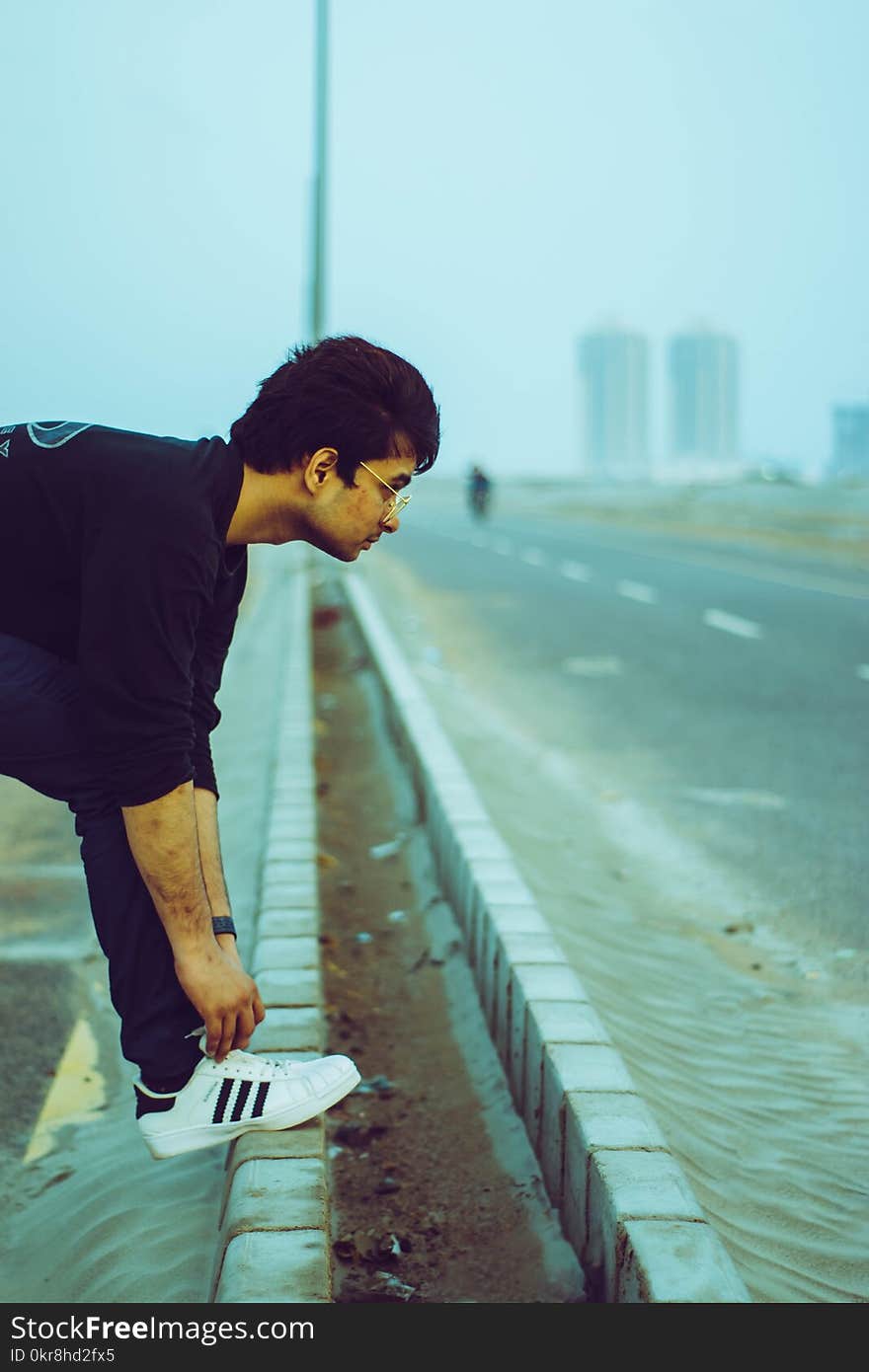 Man in Black T-shirt and Blue Denim Jeans Lacing His Shoes