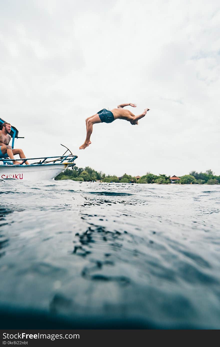 Man Wearing Blue Shorts Performing Back Flip over Body of Water