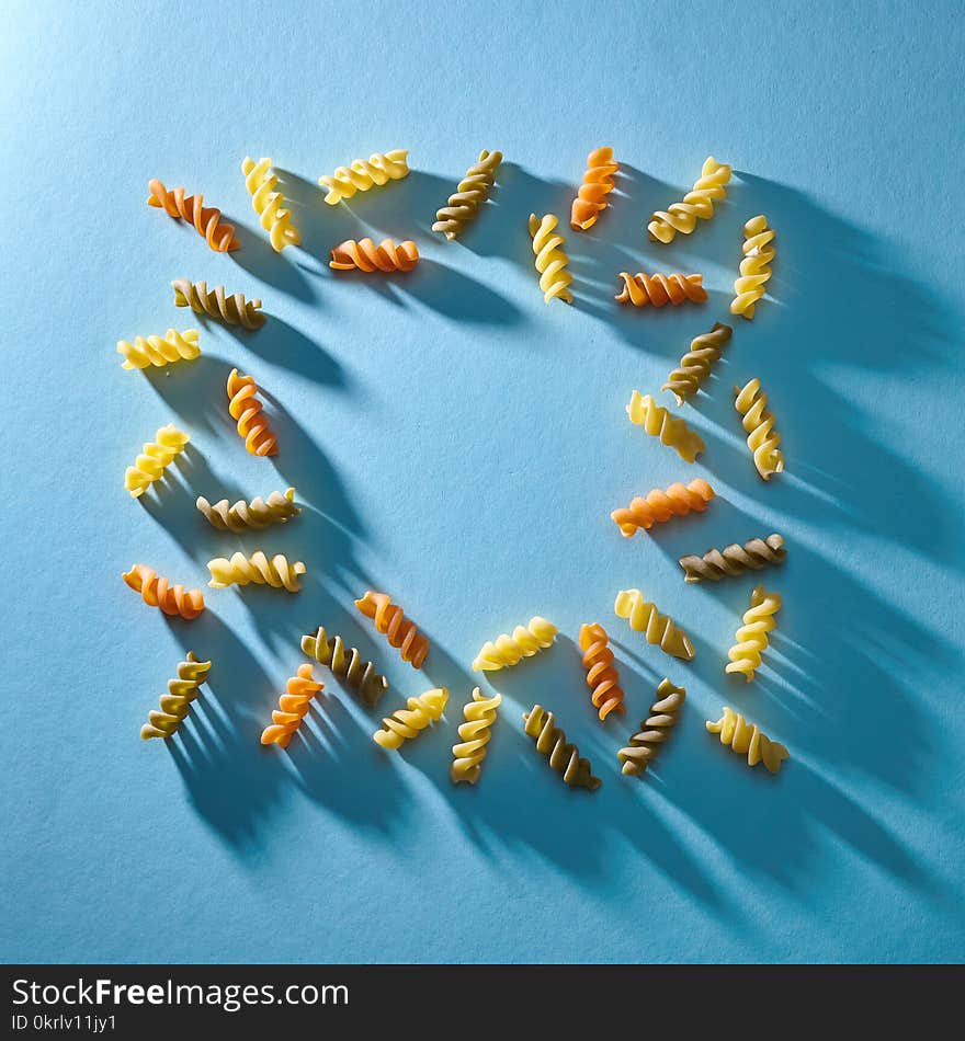 Frame in the shape of a square of multicolored pasta on a blue background. Flat lay.