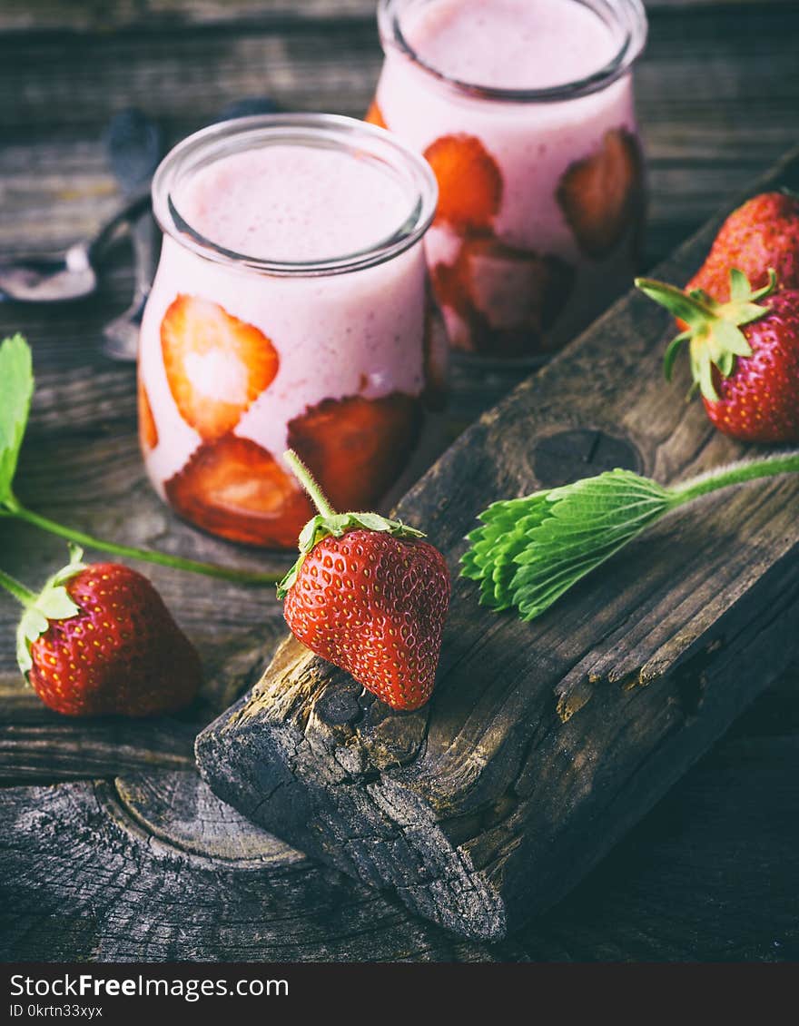 A ripe red strawberry and two glass jars of smoothies on a gray wooden table