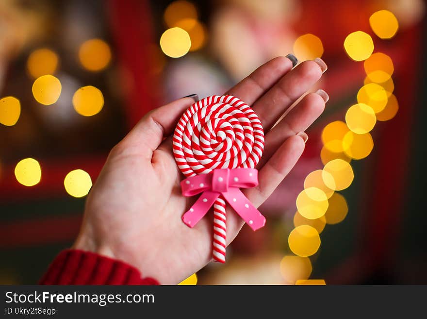 Close up christmas lollipop on woman`s hand on a background of colored lights. Close up christmas lollipop on woman`s hand on a background of colored lights.