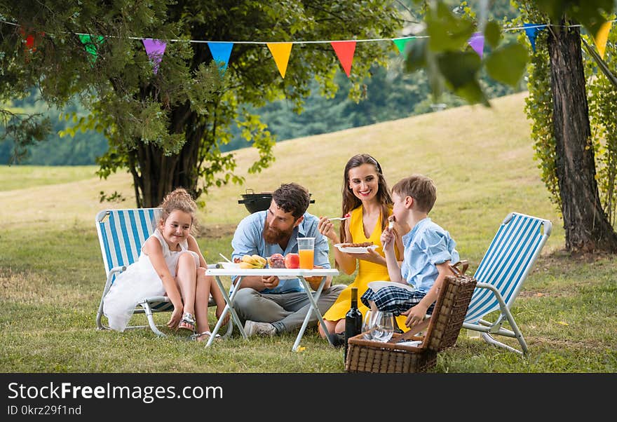 Dedicated young parents of two children listening to their funny son talking while eating together during family picnic in a summer day. Dedicated young parents of two children listening to their funny son talking while eating together during family picnic in a summer day