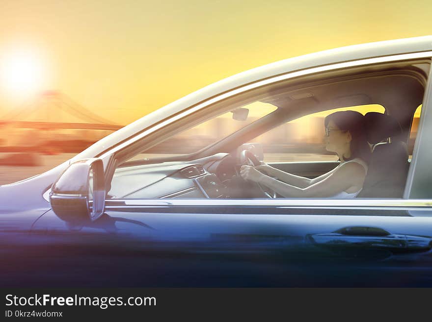 Younger woman driving passenger car in urban against sunset sky