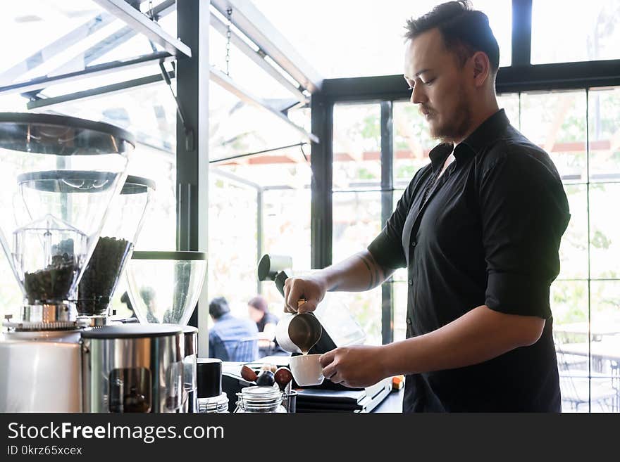 Serious bartender pouring fresh milk into a cup of coffee