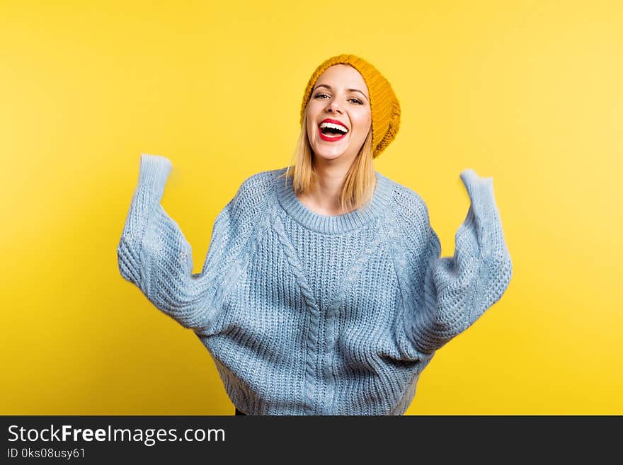 Portrait of a young beautiful woman with a woolen sweater and a hat in studio on a yellow background, having fun. Portrait of a young beautiful woman with a woolen sweater and a hat in studio on a yellow background, having fun.