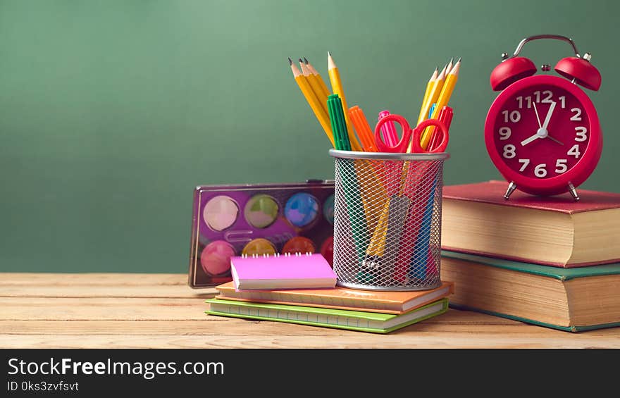 Back to school concept with alarm clock, pencils and old books on wooden table