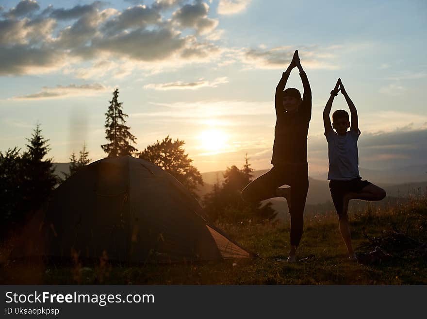 Young mother and son doing gymnastics at the mountains at sunset. Mother and son doing yoga. Woman and child training in the nature. Outdoor sports. Healthy sport lifestyle.