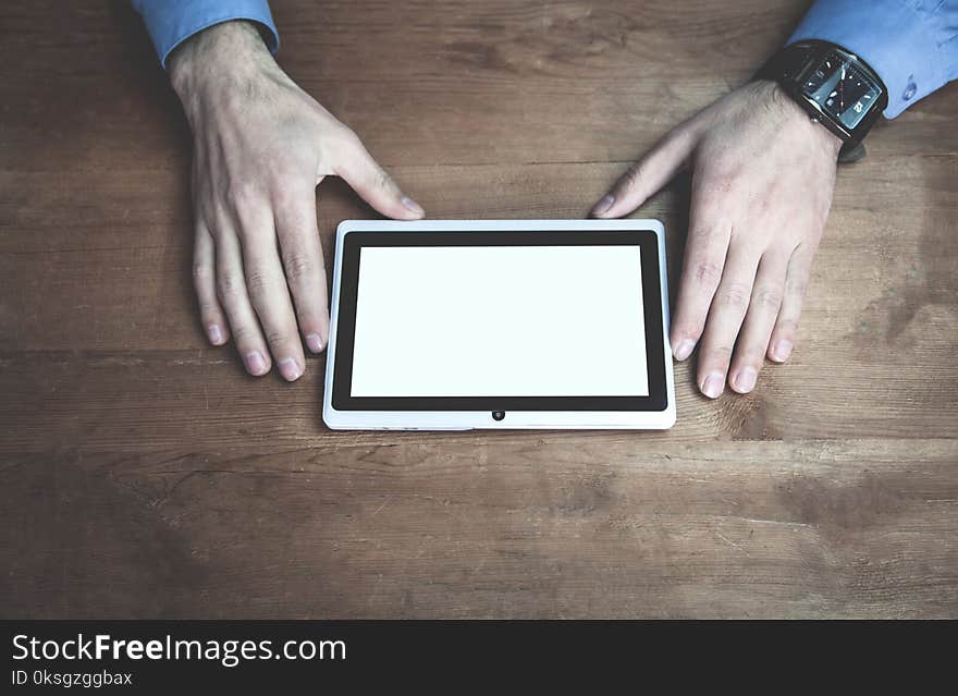 Hands using tablet white screen display on wooden desk.