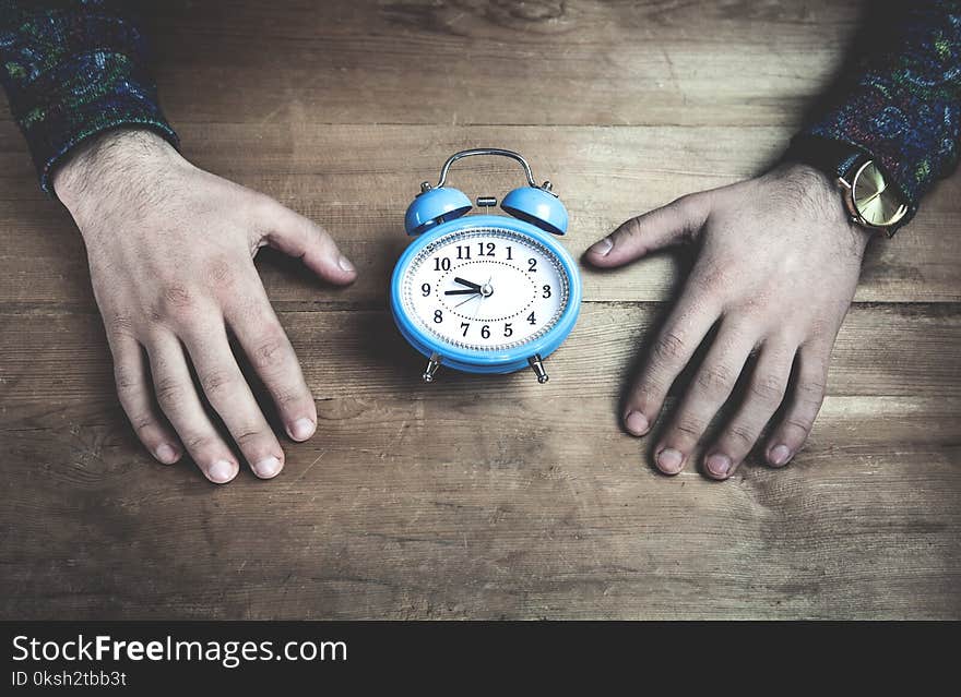 Hands holding blue alarm clock on wooden table.