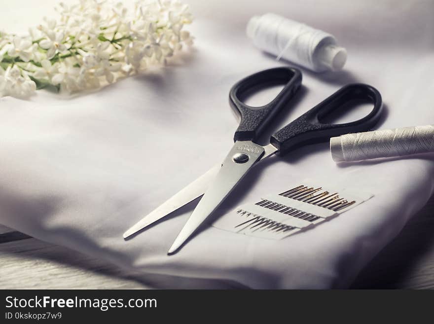 Background with sewing tools. Scissors, bobbins with thread and needles and textile on white table.