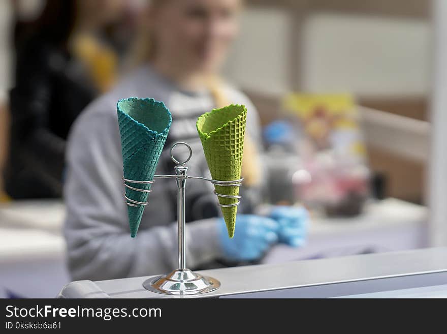 Unrecognizable young saleswoman and two empty bright wafer sweet cornets for ice cream, waffle cones, Real scene in store. Selective focus, for background use. Unrecognizable young saleswoman and two empty bright wafer sweet cornets for ice cream, waffle cones, Real scene in store. Selective focus, for background use