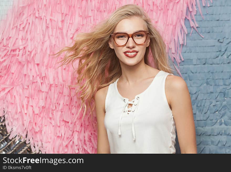 Portrait of a young blonde woman with long hair in stylish glasses toothy smiling and looking at camera. Studio shot. Portrait of a young blonde woman with long hair in stylish glasses toothy smiling and looking at camera. Studio shot