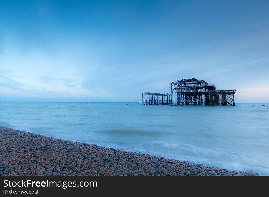 Old Brighton Pier viewed from the pebble beach with the waves rolling in on a sunny day. Old Brighton Pier viewed from the pebble beach with the waves rolling in on a sunny day