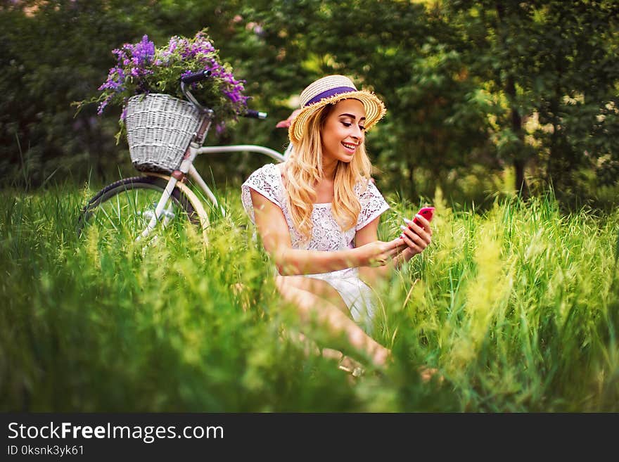 Beautiful young girl with vintage bicycle and flowers on city background in the sunlight outdoor.