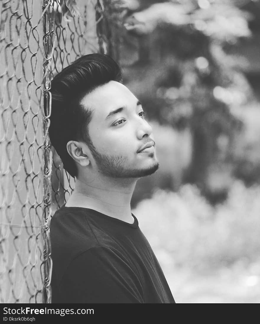 Grayscale Photo of Man Leaning on Wire Fence