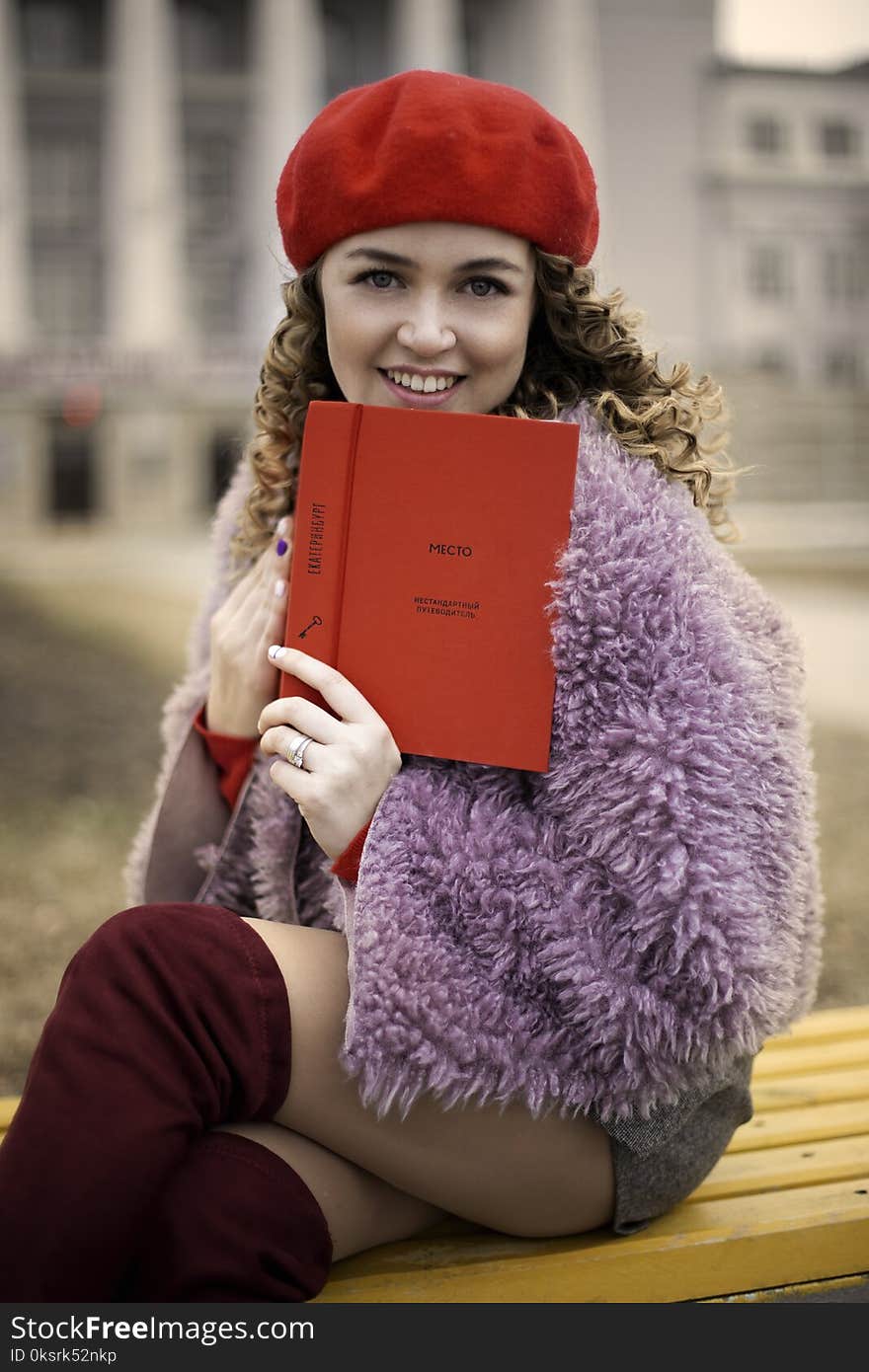 Woman Wearing Purple Coat and Gray Shorts Sitting on Brown Chair