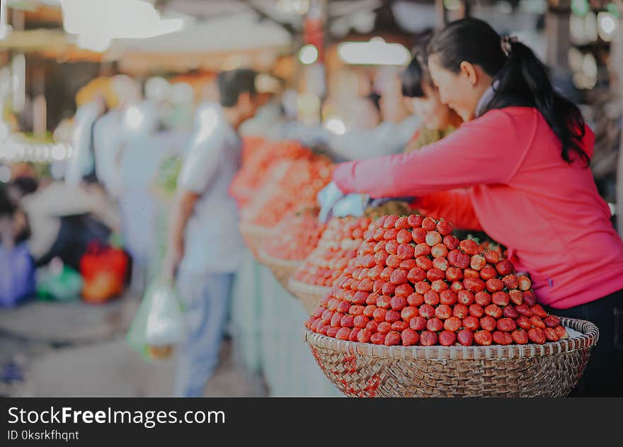 Selective Focus Photography Of Woman Wearing Red Hoodie Standing Behind Of Basket Full Of Fruits