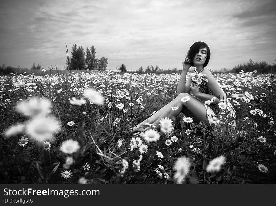 Grayscale Photo of Woman Sitting Beside Daisies