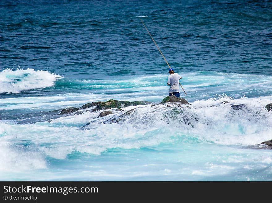 Man In White Shirt Holding A Fishing Rod While Standing On Rock