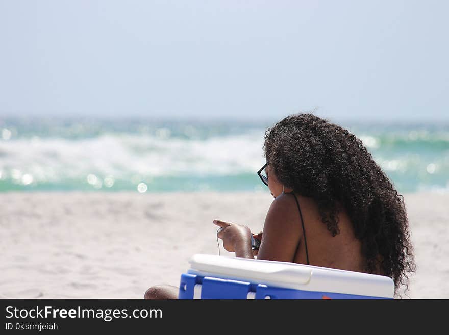 Woman Sitting on Sand Beside Blue and White Cooler Box Near Shore