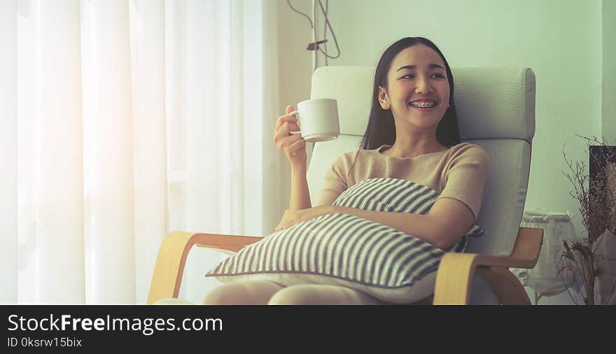 Smile Asian girl on sofa sitting and drinking coffee by the windows