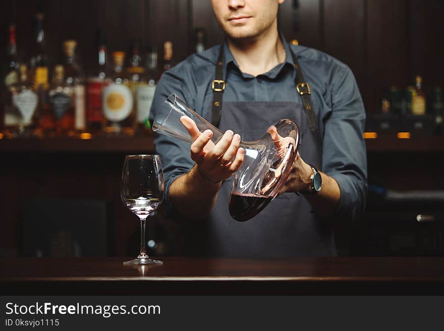 Sommelier pouring wine into glass from mixing bowl. Male waiter