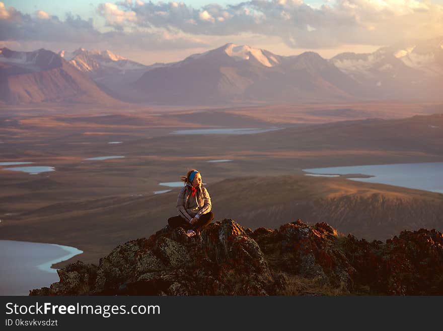 Girl sits on big rock against mountains and lakes