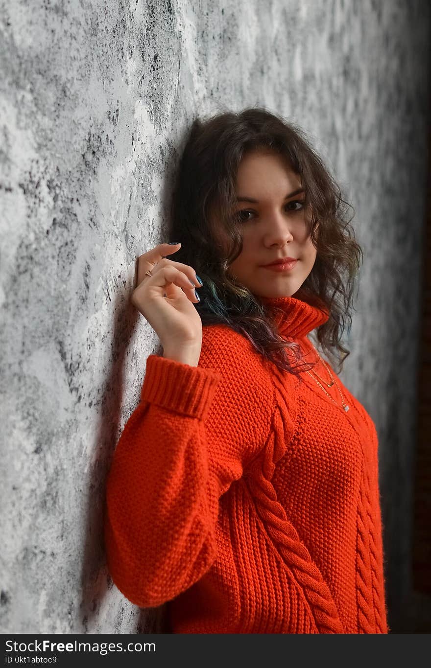 Sensual beautiful girl posing in red sweater. Girl with long curly hair.