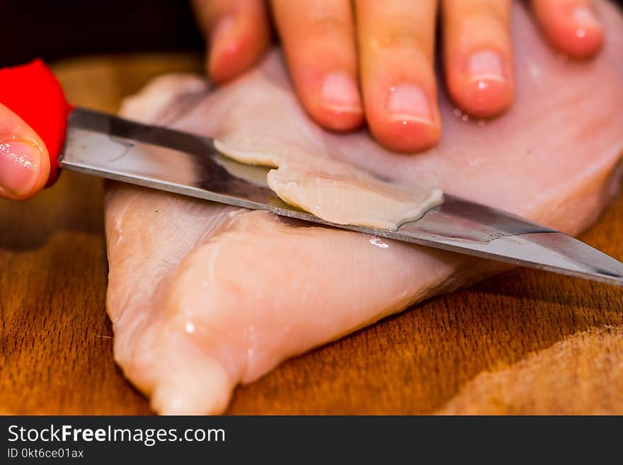 Woman cutting the chicken breast by knife on the wooden board