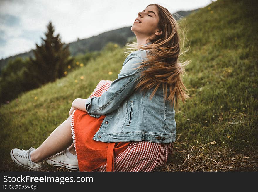 Woman Wearing Blue Denim Jacket Sitting on Green Grass Near Trees Under Blue Sky at Daytime