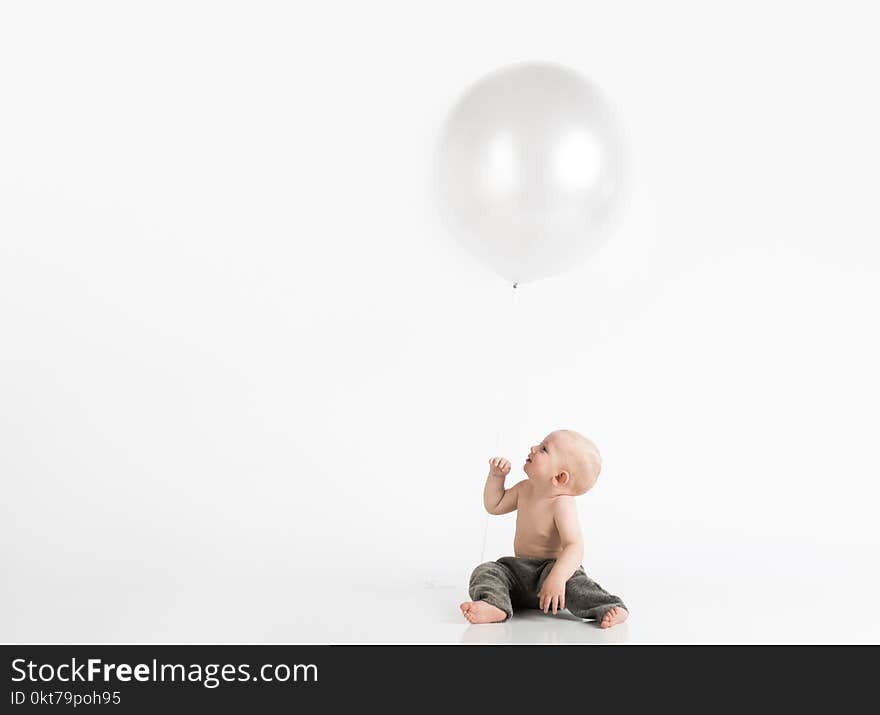 Topless Toddler With Pants Sitting on White Surface While Looking Up