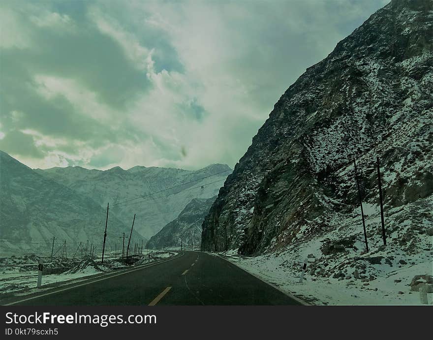 Snow Covered Mountain Ranges Near the Asphalt Road Under the Cloudy Sky