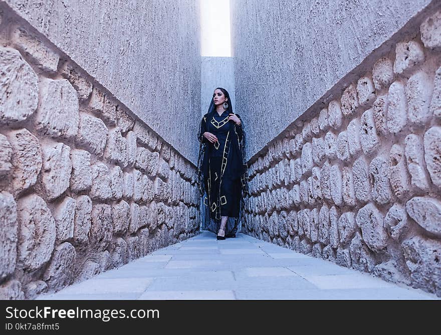 Woman in Black and Gold Traditional Dress Between Gray Concrete Walls