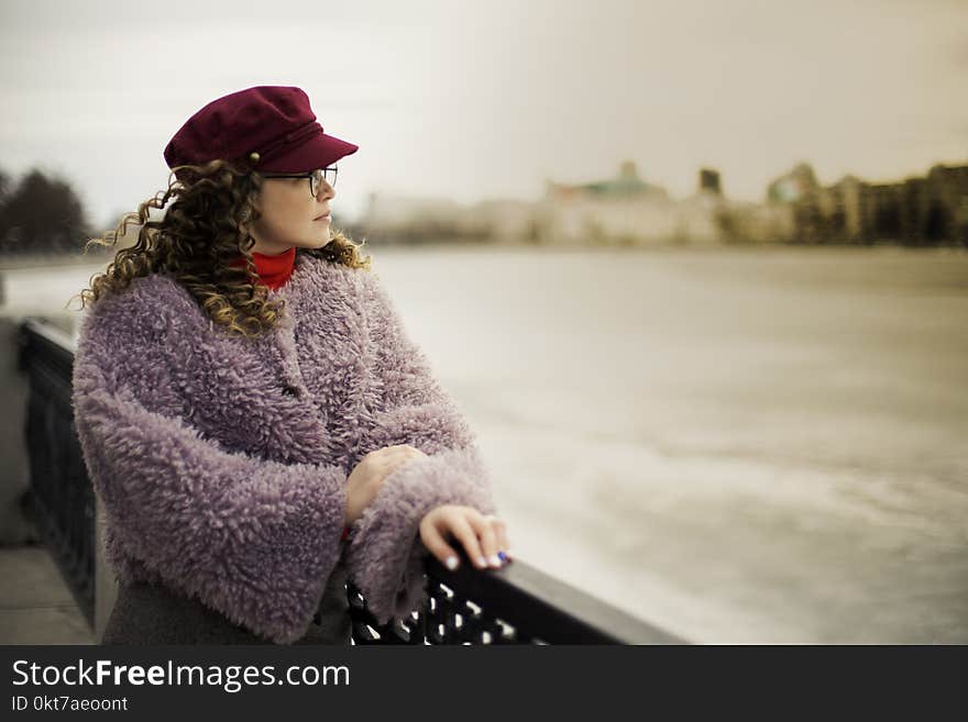 Woman Wearing Purple Fleece Coat Standing Beside Black Metal Fence Near Body of Water