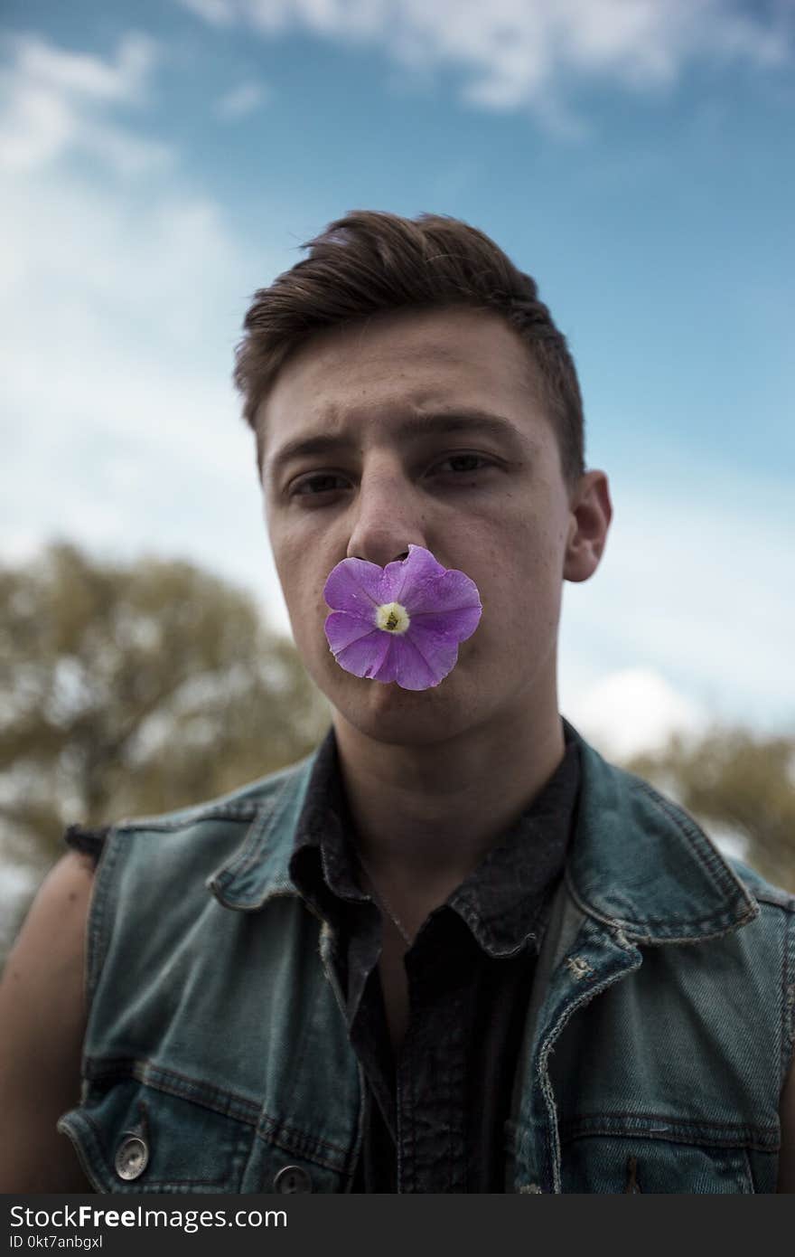 Man in Blue Denim Collared Vest With Purple Flower on Mouth