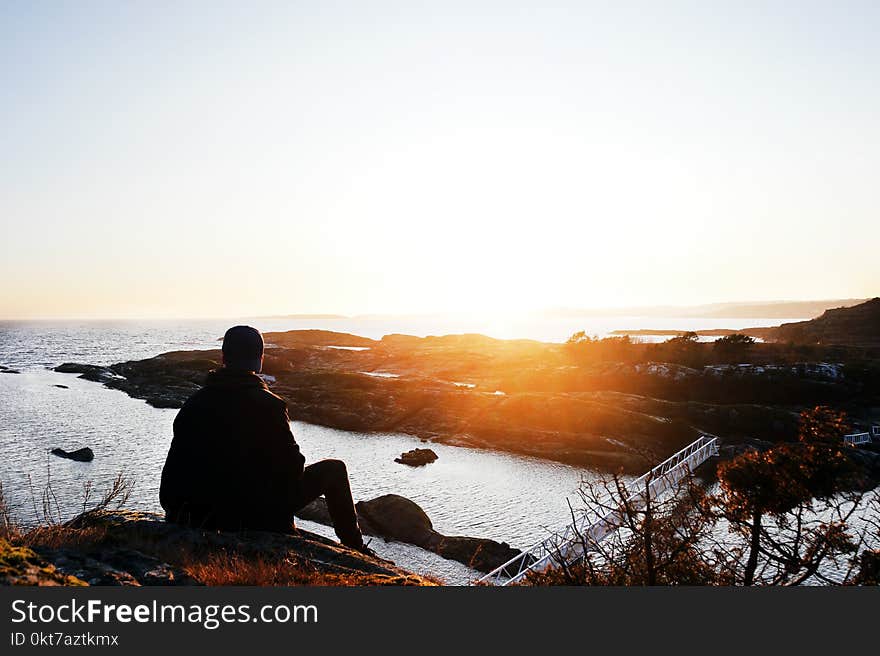 Silhouette Photo of Person Sitting Near Cliff during Golden Hour