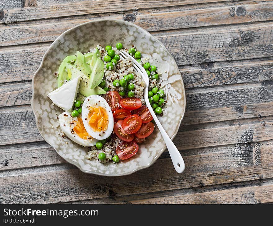 Bowl with quinoa, egg, avocado, tomato, green pea. Healthy diet food concept. Top view, on wooden background