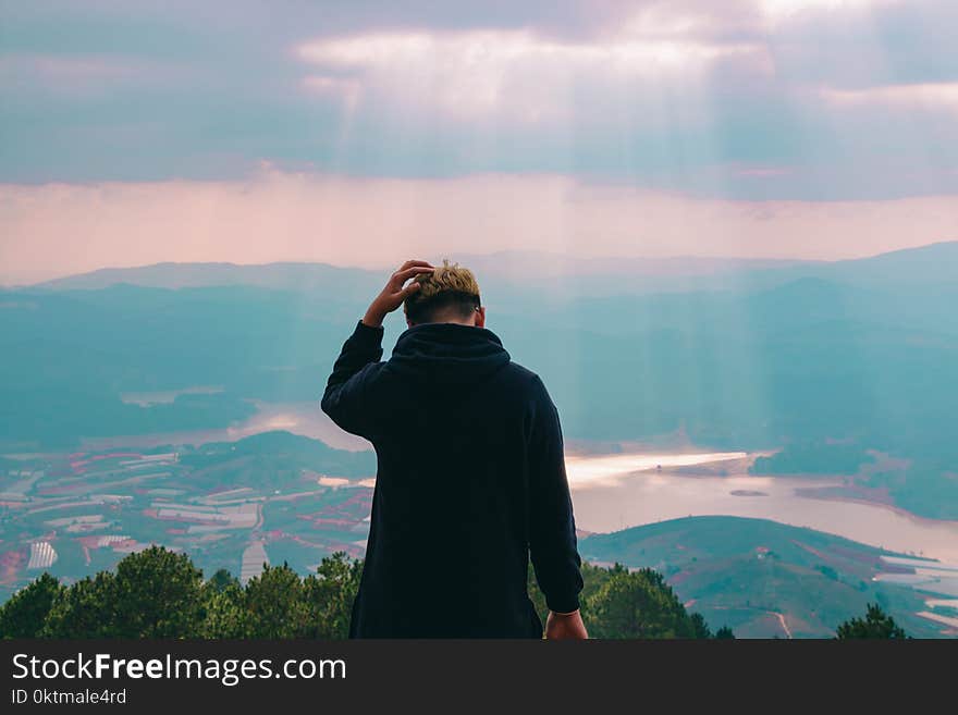 Man in Black Jacket Holding His Hair Facing Body of Water