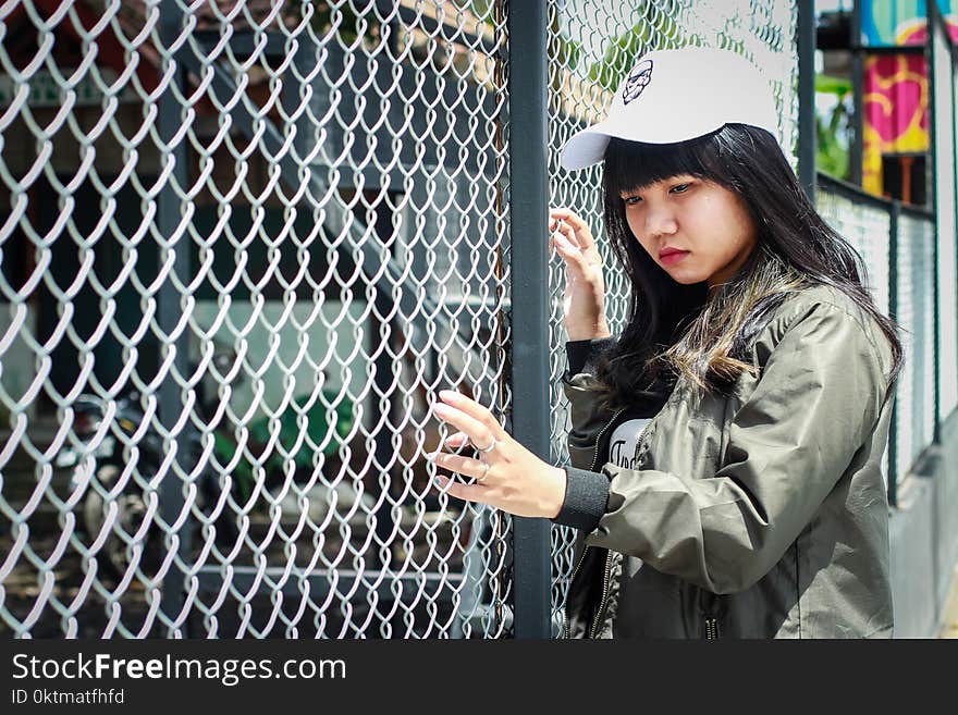 Woman Wearing Grey Bomber Jacket Leaning Near Grey Wire Fence