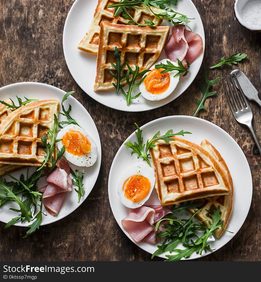 Delicious savory breakfast on a wooden background - boiled eggs, potato waffles and ham, top view